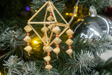 Christmas tree with straw ornament and silver bauble. Traditional holiday tree with geometric straw ornament and warm lights creating cozy seasonal ambiance.の写真素材