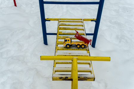 Yellow toy truck on a snowy playground ladder. Forgotten childhood memories concept with a bright...