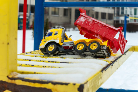Yellow toy truck on a snowy playground ladder. Forgotten childhood memories concept with a bright...