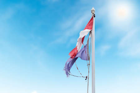 Thai flag torn and with knots in the wind on blue skyの写真素材