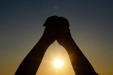 Human's hand praying, meditating in harmony and peace at sunset. Religion, spirituality, prayer,...