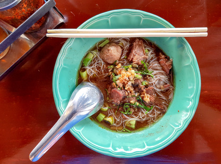 White slim noodle soup with meatball and pork stewed served in a green bowl.