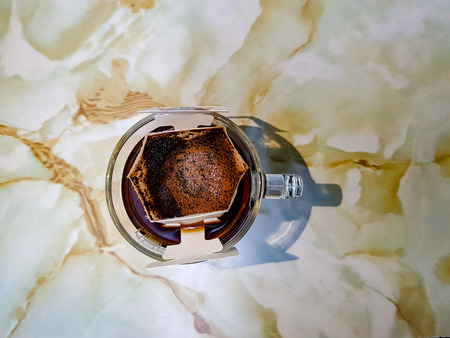 Drip fresh coffee sachets on the transparent glass coffee cup with dripped coffee inside.の写真素材