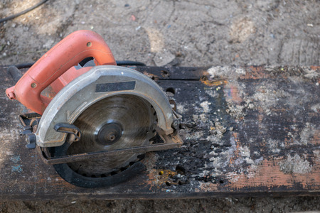 An electrical portable  circular saw with orange handle on the old and dirty plankの写真素材