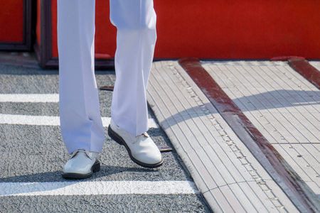 Navy officer in summer white uniform walks on main deck of naval ship with special equipment to handling helicopter. just only trousers and shoes.の写真素材