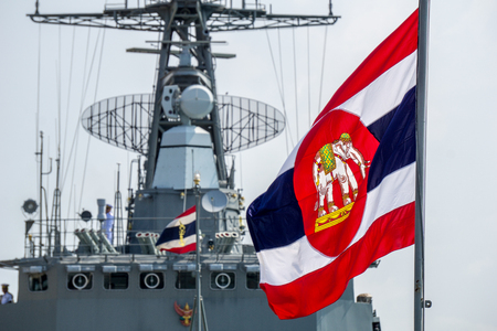 CHONBURI, THAILAND - MARCH 15, 2018 : Royal Thai Navy ensign blow on flag pole with Royal Thai Navy Frigate in the background on March 15, 2018 in Lamthien Naval Base, Chonburi, Thailand.のeditorial素材