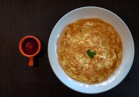 Yellow fried chicken eggs  or omelet served in white plate with tomato sauce bowl on the table cloth