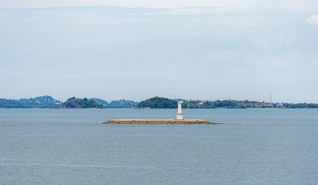Small white beacon is on the artificial isle to mark the dangerous rocks below the surface with an island in the backgroundの写真素材