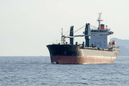 Old commercial cargo ship with heavy cranes anchors in the sea.の写真素材