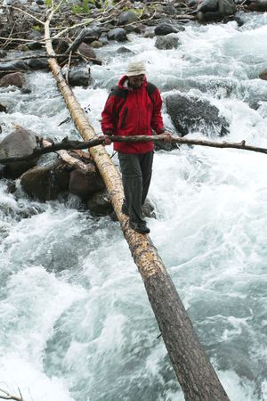Man going up along log for wild riverの写真素材