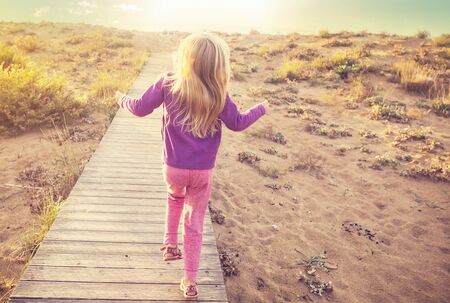 Little girl goes by boardwalk in sea shore at sunriseの写真素材