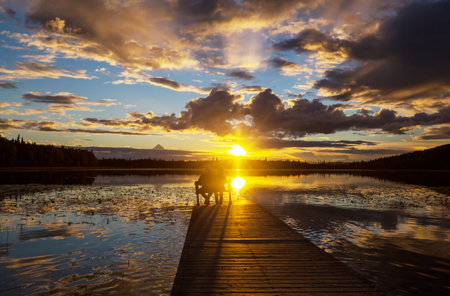 Couple resting at ease by the calm lake at sunset. Relaxation vacationの写真素材