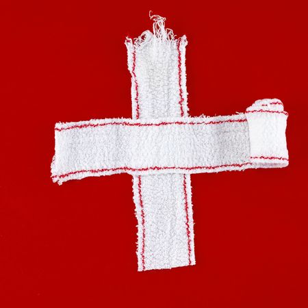 cross made of white bandages on a red chalk backgroundの写真素材
