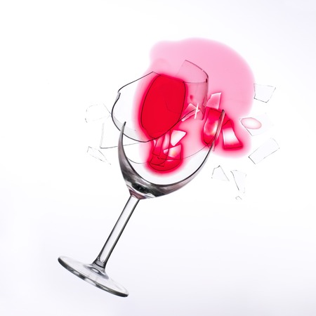 fallen wine glass with red wine in it and red stain on a white tableclothの写真素材