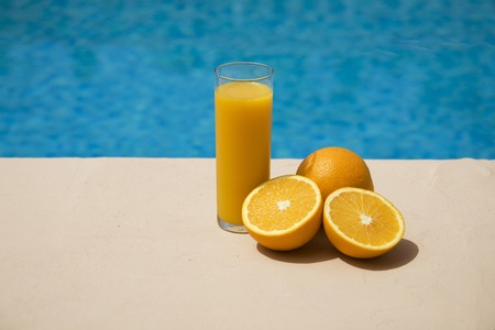 glas with orange juice and oranges at the swimming pool sideの写真素材