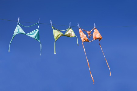 Three colorful bikini tops drying on washing line (blie sky, summer vacation concept)の写真素材