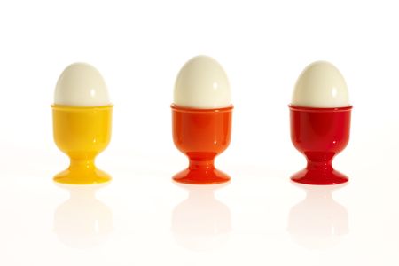 three eggs in colorful egg cups (yellow, orange, red, white backfround)