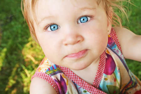 Adorable little girl with big blue eyes on a grass backgroundの写真素材