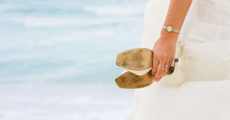 Bride looking at the sea with shoes in handsの写真素材