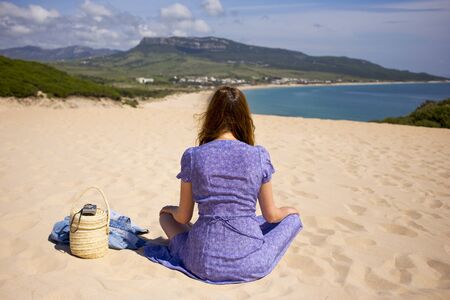 A woman sitting is on a beach near ocean with a basket.の写真素材