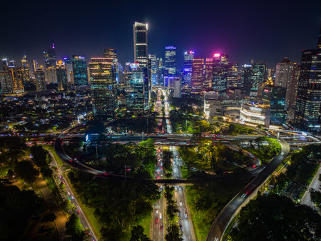 Aerial drone view of Jakarta city skyline at night with illuminated skyscrapers, glowing cityscape, and busy traffic in Indonesia. Modern urban life in Southeast Asia.の写真素材