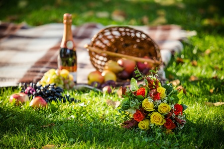 Wker basket with bouquet of flowers, bottle wine on the grass.の写真素材