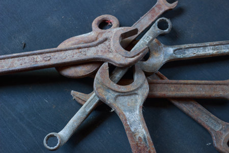 A close-up of weathered, rusty wrenches and a hook on a dark surface, showcasing their aged texture...
