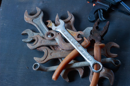 A close-up of weathered, rusty wrenches and a hook on a dark surface, showcasing their aged texture...