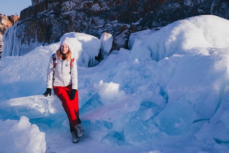 Traveling woman sitting on the blocks of ice. Winter tourism in Russia Baikal Lake. Winter ice along...