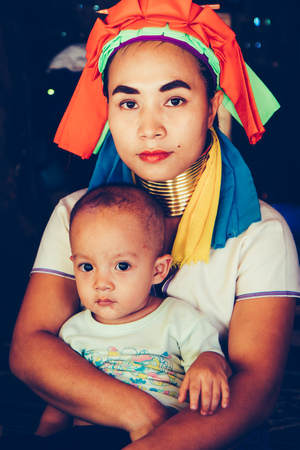 Long Neck Woman wearing at traditional costume is sitting with her child. Tribal village Northern Thailand.の写真素材