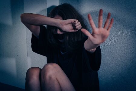 A woman suffers from violence. She sits on the tiled floor with her face bent and her hand out.の写真素材
