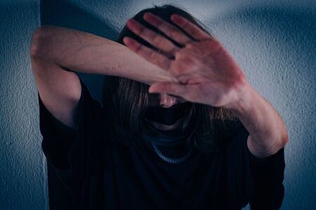 A woman suffers from violence. She sits on the tiled floor with her face bent and her hand out.