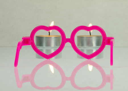 Pink glasses in the shape of hearts and candles visible in the distance.の写真素材