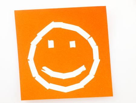 Orange Sticky note with the symbol of a happy face drawn with the correction tape.の写真素材