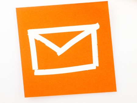 Orange Sticky note with email symbol drawn with the correction tape.の写真素材