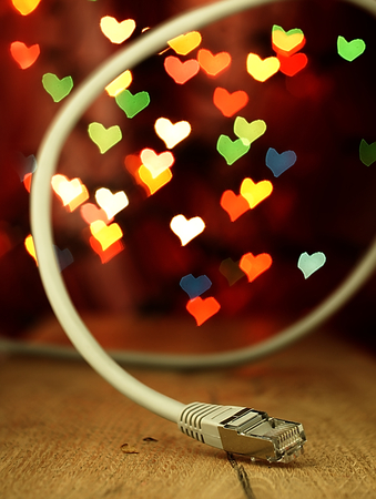 Network cable on a wooden surface of the table with blurred hearts in the background.