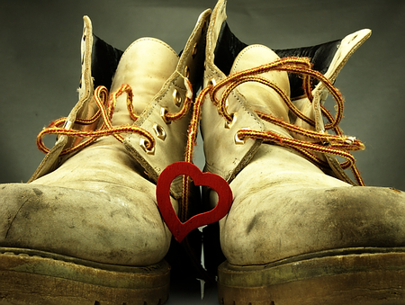 Old pair of heavy military boots and red delicate heart between them.の写真素材