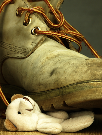 Teddy bear under the old, dirty and heavy military boot. The view from the perspective of frogs.の写真素材