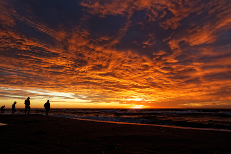 Sunset and dramatic clouds over the sea casts a glow on some indistinct human figures.の写真素材