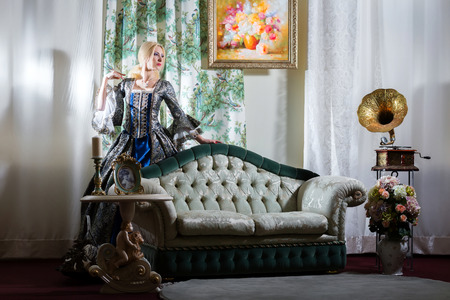 Girl in medieval dress standing next to the sofaの写真素材