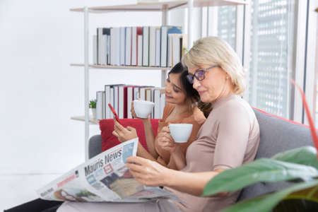 Mother and her adopted daughter are drinking coffee in the living room together happily.Unusual appearance, diversity, heredity concept.のeditorial素材