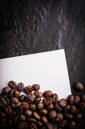 roasted coffee beans with blank paper on dark background, can be used as a backgroundの写真素材