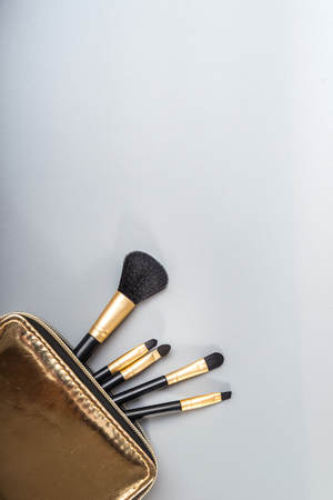 Make up brushes spilling out of a gold cosmetics bag on pastel color background.Top view. Flat lay. Beauty concept.の写真素材