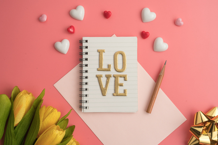 Flat view of notepads with love alphabet in the centre of valentines hearts and decoration on pink background with copy space. Symbol of love. Happy Valentines Day background.Saint Valentine's Day concept. Can be used for celebrations valentines day.の写真素材