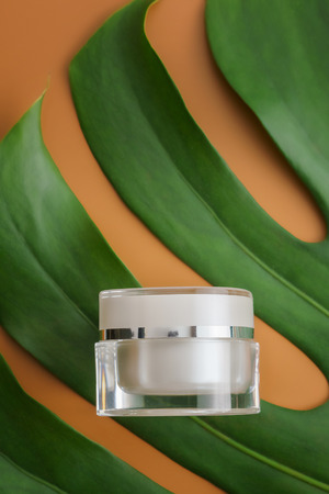 White cosmetic products and green leaves on brown color background. Natural beauty product for branding mock-up concept.の写真素材