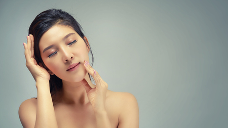 Happy beautiful asian girl with the fresh skin in grey colour background. Expressive facial expressions. Cosmetology and Spa concept.の写真素材