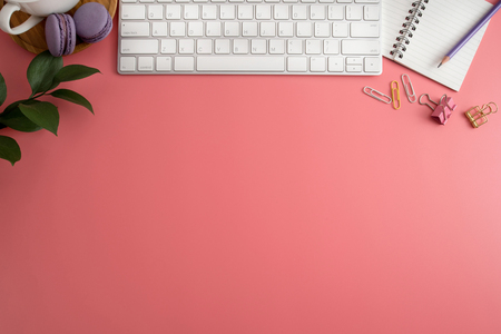 Styled stock photography pink office desk table with blank notebook, keyboard, macaroon, supplies and coffee cup. Top view with copy space. Flat lay.の写真素材
