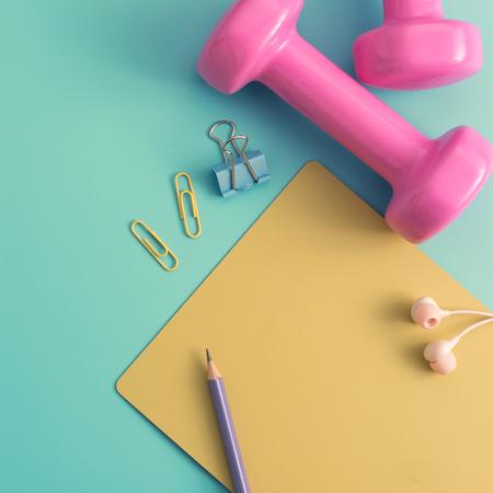 Pastel styled stock photography of fitness equipment dumbbells notepad pencil and earphone on color background. Flat lay.の写真素材