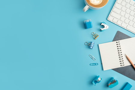 Flat lay, top view office table desk. Work space with blank note book, keyboard, blue office supplies and coffee cup on white background.の写真素材