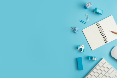Flat lay, top view office table desk. Work space with blank note book, keyboard, blue office supplies and coffee cup on white background.の写真素材